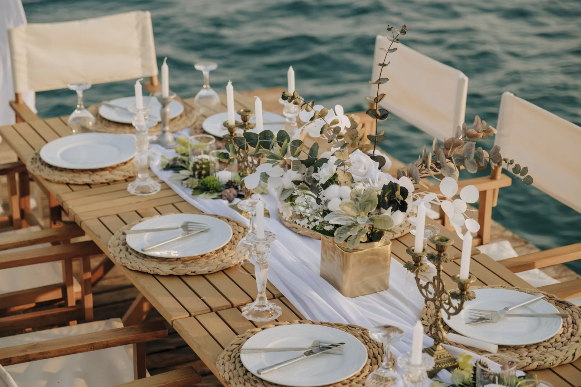 A table set with plates and candles on the water.
