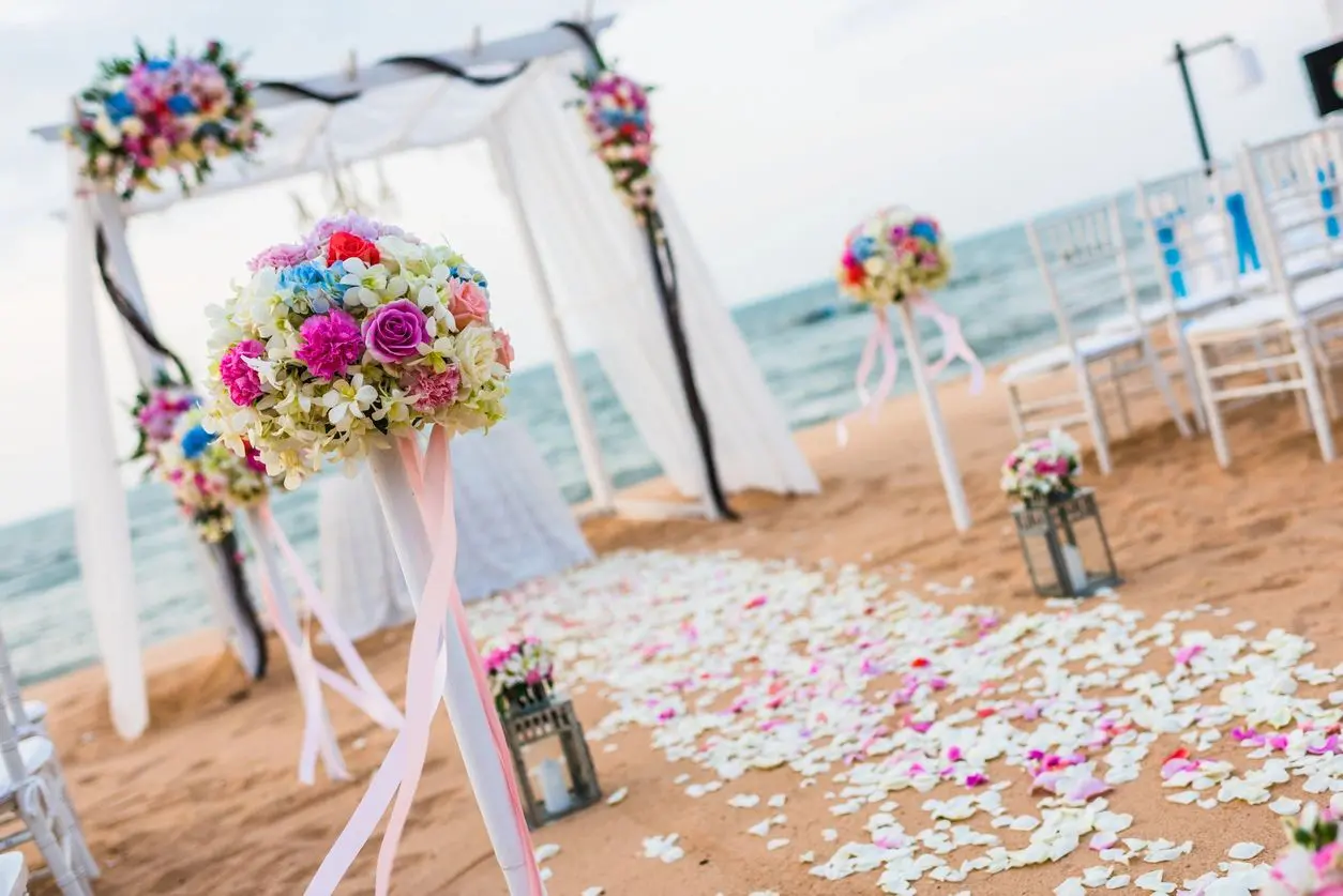 A beach wedding with flowers and candles on the sand.