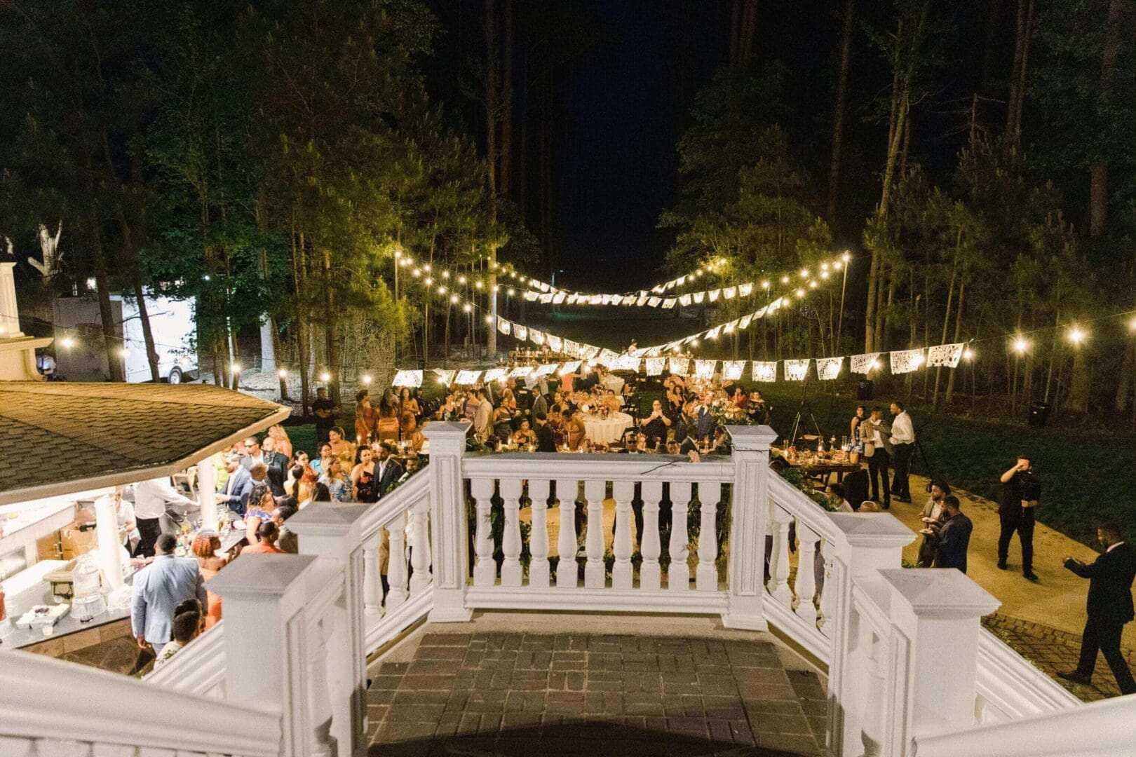 Outdoor evening event with string lights and a white decorative railing.